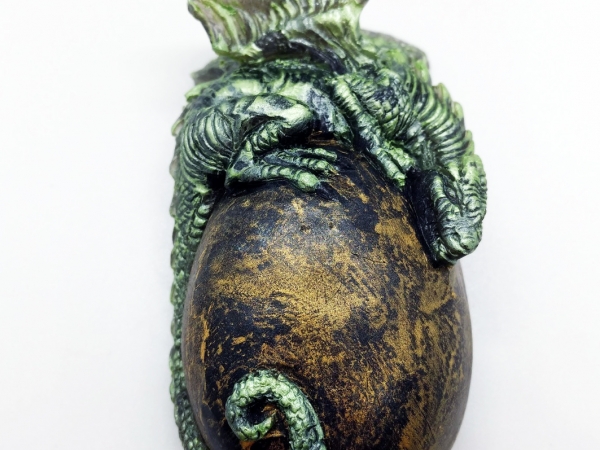 A green baby dragon rests on top of a golden egg.
