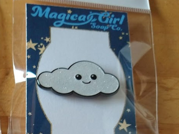 A photo of an enamel pin shaped like a cloud with a happy face.