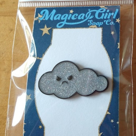 A photo of an enamel pin shaped like a cloud with a grumpy face.