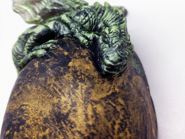 A green baby dragon rests on top of a golden egg.