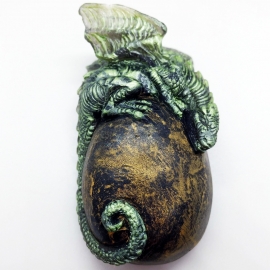 A green baby dragon rests on top of a golden egg.
