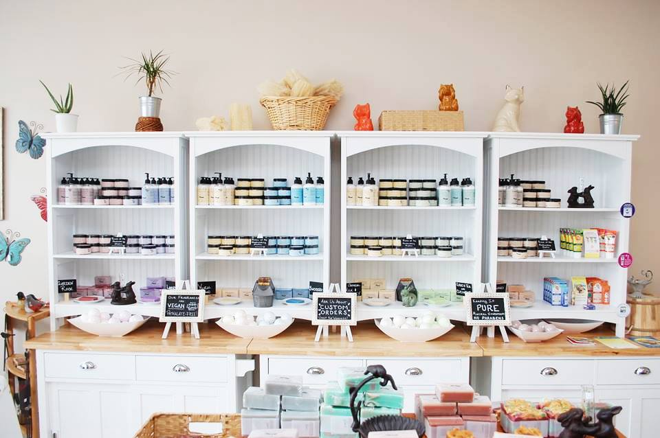 A view of our former boutique: four white shelves with a variety of bath care products artfully displayed. 